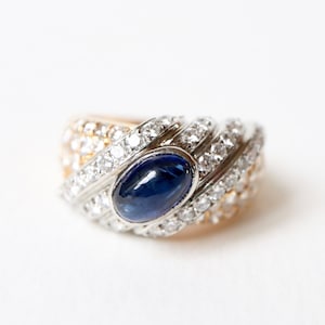 May include: A gold and silver ring with a blue gemstone surrounded by diamonds.
