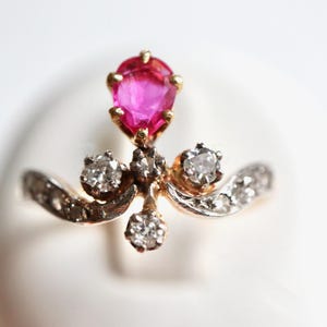 Può includere: Un anello d'oro con una gemma rosa brillante a forma di pera e diamanti scintillanti. L'anello ha un design ornato con una fascia delicata e curva. Il design dell'anello ricorda una corona. Un gioiello.