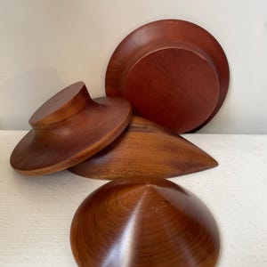 Op de afbeelding: Een verzameling handgemaakte houten kommen en decoratieve objecten. De items zijn gemaakt van donker hout met een gladde, gepolijste afwerking. De vormen omvatten een grote kom, een bord en verschillende unieke, conische vormen.