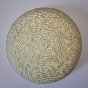 Può includere: Un cesto rotondo intrecciato di colore bianco sporco naturale. Il cesto presenta un motivo a spirale al centro e un bordo decorativo. La trama fitta suggerisce durata e un'estetica artigianale.