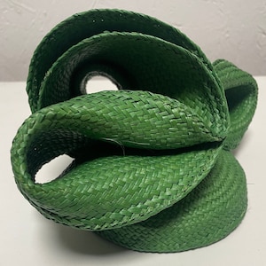 May include: A green woven hat with a unique, twisted design. The hat is made of a tightly woven material and has a smooth, rounded shape.