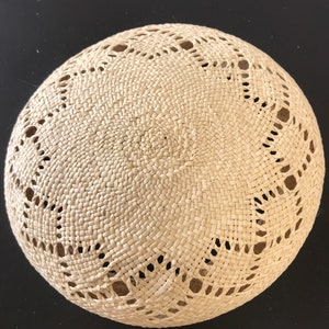 Può includere: Un cappello rotondo di paglia intrecciata con un motivo traforato decorativo attorno al bordo.