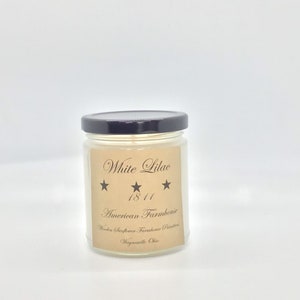 Peut inclure: Une bougie en verre dans un pot avec un couvercle noir. L'étiquette est brune avec du texte blanc qui dit "White Lilac 1811 American Farmhouse Wooden Sunflower Farmhouse Scented Waynesville Ohio".