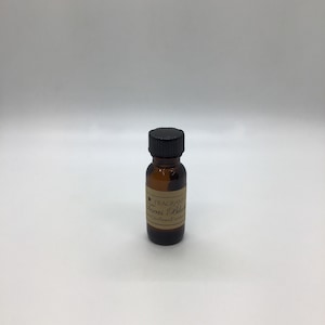 May include: A small amber glass bottle with a black cap. The label reads "FRAGRANT Texas Bluebonnet" with a star graphic. The bottle contains a liquid, likely an essential oil or fragrance. The background is plain white.