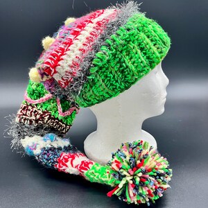 May include: A green, red, white, and black crocheted elf hat with a long, colorful tail and a multi-colored pom-pom.