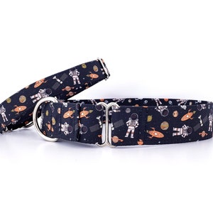 May include: Two dog collars with a space-themed pattern. The collars are black with a repeating design of astronauts, rockets, planets, and stars in orange, white, and gray. The collars have silver metal hardware.