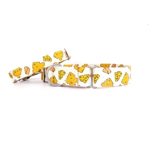 Pode incluir: Um conjunto de coleira e trela para cães. O conjunto apresenta um padrão repetido de fatias de queijo amarelo sobre um fundo creme. A coleira tem uma fivela e um anel em D de metal prateado. A largura da coleira é de aproximadamente 2,5 cm.