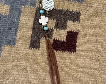 Op de afbeelding: Een bruine leren kwast sleutelhanger met een witte kruis charme en een zilveren charme die "Bless this horse & rider and keep them safe" zegt.