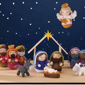Può includere: Un presepe all'uncinetto con una Maria blu e bianca, un Giuseppe marrone, un Gesù bambino marrone, un asino grigio, un agnello bianco, tre re magi e un angelo con un'aureola dorata.