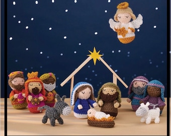 May include: A crocheted nativity scene featuring a blue and white Mary, a brown Joseph, a brown baby Jesus, a grey donkey, a white lamb, three wise men, and an angel with a gold halo.