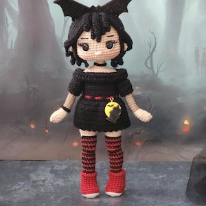 May include: A black crocheted doll with black hair, wearing a black dress with red accents, black and red striped stockings, and red shoes. The doll has a bat headband and a yellow bat charm.