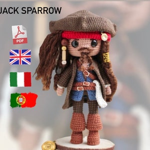 Può includere: Bambola amigurumi all'uncinetto di Jack Sparrow del franchise di film Pirati dei Caraibi. La bambola indossa un cappello marrone, una bandana rossa, una giacca marrone, una camicia blu, pantaloni marroni e stivali marroni. La bambola ha una barba e baffi marroni e capelli marroni. La bambola è in piedi su una base di legno. L'immagine include il testo "JACK SPARROW" e un'icona PDF.