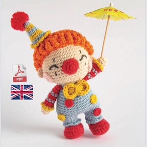 Può includere: Bambola clown amigurumi all'uncinetto con naso rosso, papillon giallo e vestito a righe blu e bianche. Il clown tiene un ombrello di carta giallo e rosso.