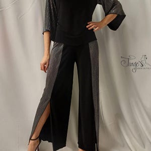 May include: Black dance trousers with a silver sequined design on the sides. The trousers have a wide leg and a slit on the side. The trousers are paired with a black top with a cowl neck and silver sequined sleeves. The top has a fitted bodice and a loose, flowing sleeve.