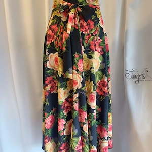 Könnte beinhalten: Schwarzer Wickelrock mit einem lebendigen Blumenmuster mit rosa, roten und gelben Rosen. Der Rock hat eine passende Schleife an der Taille und wird mit einem schwarzen Oberteil kombiniert. Das Tango's Made in Italy-Logo ist sichtbar.