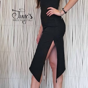 May include: A woman wearing a black dress with a side slit and a gold pair of heels. The dress has a strap that goes over the shoulder and a small ruffle detail. The woman is standing in front of a white slatted wall. The text "Tango's Made in Italy" is visible in the lower left corner of the image.