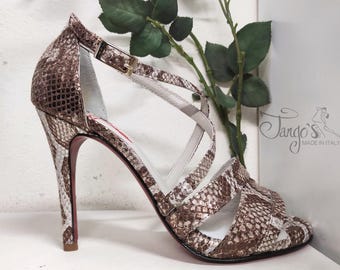 May include: A pair of brown and white snakeskin heeled sandals with a criss-cross strap design. The sandals have a red heel and a peep toe.