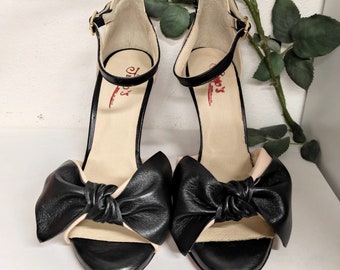 May include: A pair of black and beige heeled sandals with a large black bow on the front of each shoe. The shoes are made by Tango's, Made in Italy.