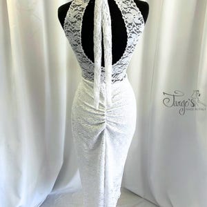 May include: White lace dress with a halter neckline and open back. The dress features a bow at the neck and a ruched design down the back. The dress is displayed on a mannequin. The Tango's Made in Italy logo is visible.