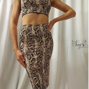 Puede incluir: Conjunto de dos piezas con estampado de piel de serpiente. El conjunto incluye un top corto con cuello en V y una falda lápiz hasta la rodilla. El estampado presenta tonos marrones, beige y negros. El conjunto es ajustado y parece estar hecho de un material elástico.