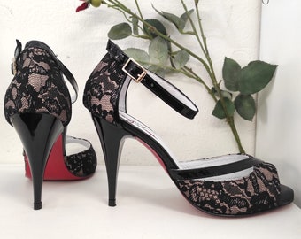 Op de afbeelding: Een paar zwarte sandalen met hak, peeptoe en enkelband. De hakken zijn zwart en de zolen zijn rood.