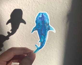 May include: A blue and white whale shark sticker with a spotted pattern. The sticker is on a white background.