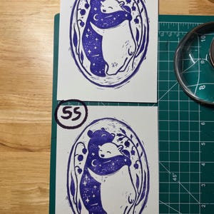 Pu&ograve; includere: Due stampe rettangolari su carta bianca con un'illustrazione a inchiostro blu scuro di due orsi che si abbracciano all'interno di una cornice ovale. L'orso a sinistra &egrave; riempito di stelle e una luna crescente, mentre quello a destra &egrave; bianco. I numeri 54 e 55 sono scritti in cerchi sulle stampe.