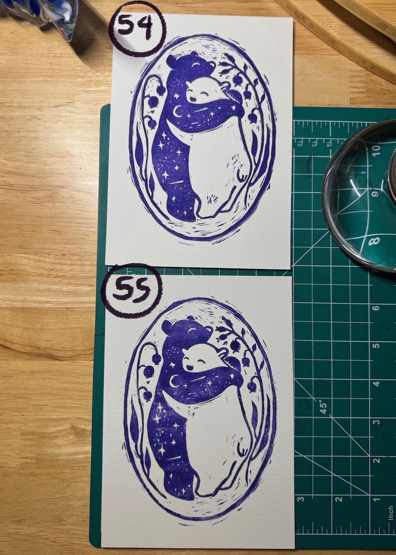 Pu&ograve; includere: Due stampe rettangolari su carta bianca con un'illustrazione a inchiostro blu scuro di due orsi che si abbracciano all'interno di una cornice ovale. L'orso a sinistra &egrave; riempito di stelle e una luna crescente, mentre quello a destra &egrave; bianco. I numeri 54 e 55 sono scritti in cerchi sulle stampe.