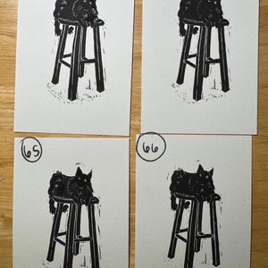 May include: Four identical black and white block prints on paper, each featuring a black cat sitting on a tall stool. The prints are numbered 63, 64, 65, and 66 in the top left corners. The artwork uses high-contrast ink lines to depict the cat.