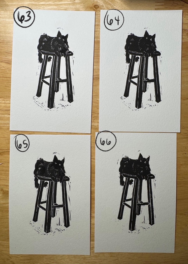 May include: Four identical black and white block prints on paper, each featuring a black cat sitting on a tall stool. The prints are numbered 63, 64, 65, and 66 in the top left corners. The artwork uses high-contrast ink lines to depict the cat.
