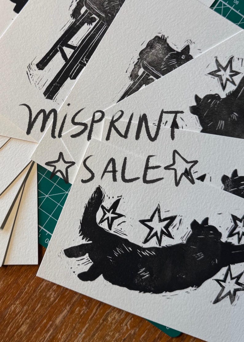 Pu&ograve; includere: Una pila di cartoline rettangolari bianche con stampe a inchiostro nero di un gatto che cerca di afferrare delle stelle. Il testo MISPRINT SALE &egrave; stampato in un carattere nero disegnato a mano sulle carte, con illustrazioni di stelle.
