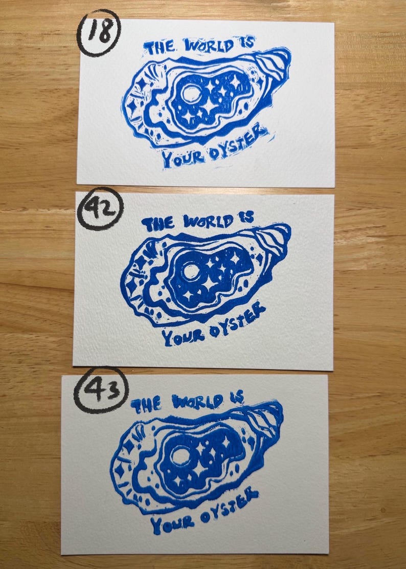 Pu&ograve; includere: Tre cartoline rettangolari bianche con una stampa a inchiostro blu di un guscio di ostrica. All'interno del guscio c'&egrave; un motivo con luna e stelle. Il testo "THE WORLD IS YOUR OYSTER" &egrave; stampato in inchiostro blu. Ogni cartolina &egrave; contrassegnata da un numero cerchiato: 18, 42 o 43.