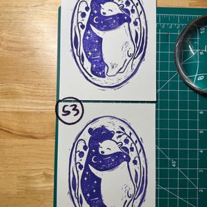 Pu&ograve; includere: Due stampe rettangolari su carta bianca con un design a stampa in blocco con inchiostro viola di due orsi che si abbracciano all'interno di una cornice ovale. L'orso a sinistra &egrave; riempito con un motivo a cielo stellato, mentre l'orso a destra &egrave; bianco.