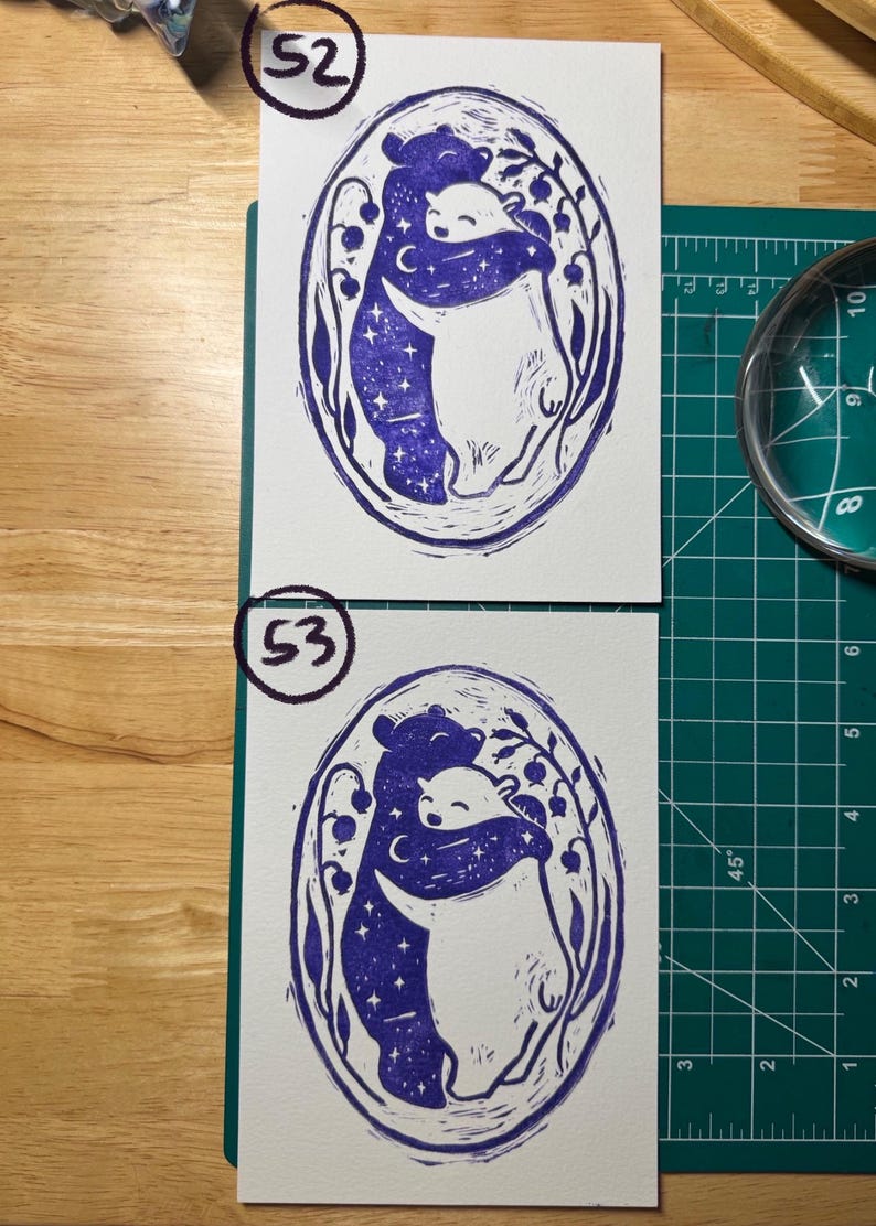 Pu&ograve; includere: Due stampe rettangolari su carta bianca con un design a stampa in blocco con inchiostro viola di due orsi che si abbracciano all'interno di una cornice ovale. L'orso a sinistra &egrave; riempito con un motivo a cielo stellato, mentre l'orso a destra &egrave; bianco.