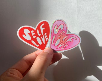 May include: Two heart-shaped stickers with the text "SELF LOVE" in a white, red, and pink color scheme. The stickers are iridescent and have a glittery finish.