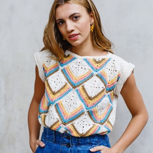 May include: A woman wearing a white crochet top with a colorful geometric pattern and a blue denim skirt with button closures.