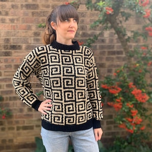 Pode incluir: Um suéter preto e creme com um padrão geométrico. O suéter tem um decote redondo e mangas compridas.