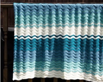 May include: A crocheted blanket with a wave pattern in shades of blue and white. The blanket is hanging on a wooden railing.