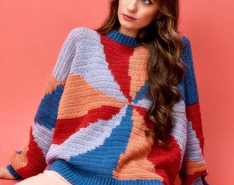 May include: A colourful crocheted sweater with a geometric pattern in shades of blue, red, orange, and purple. The sweater has a relaxed fit and a round neckline.