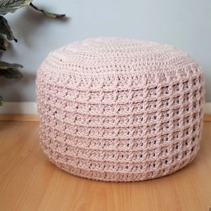 May include: A light pink crocheted ottoman footstool. The ottoman is round and has a textured surface.