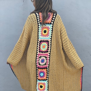 Pode incluir: Um cardigã de crochê amarelo mostarda com uma abertura frontal longa e um padrão geométrico colorido nas costas.