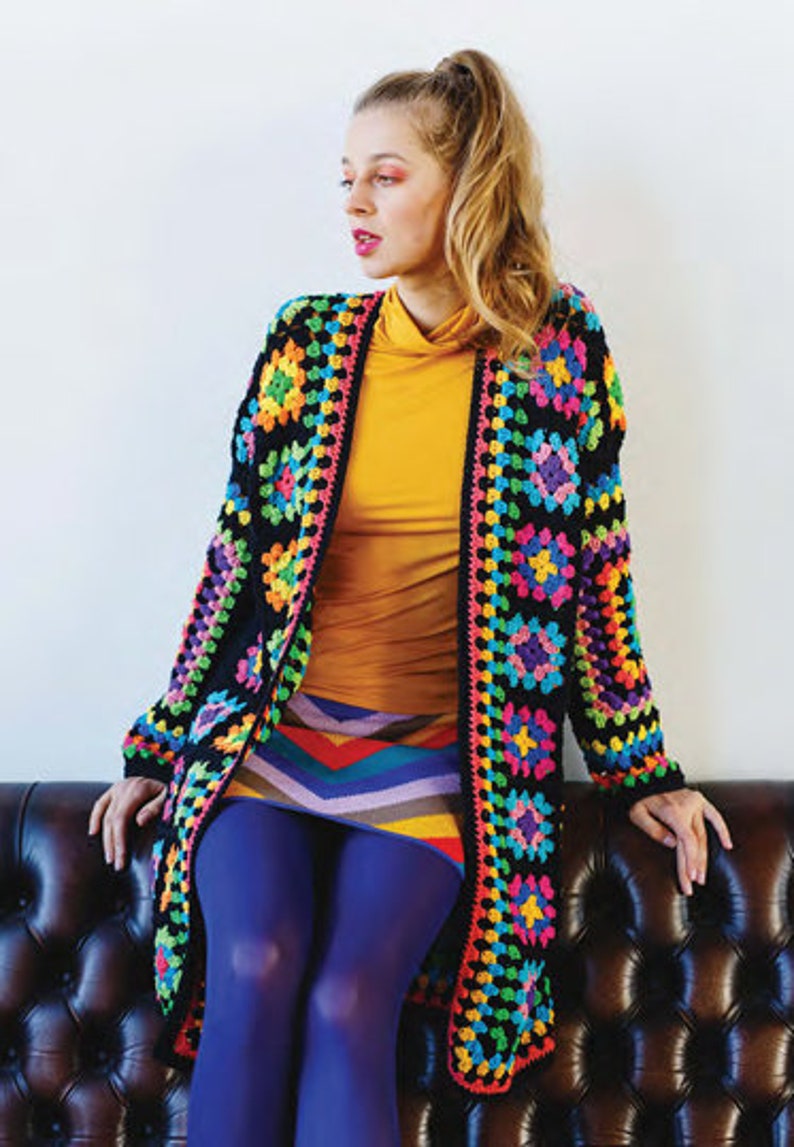 Puede incluir: Un c&aacute;rdigan de crochet negro con un patr&oacute;n geom&eacute;trico colorido. El c&aacute;rdigan est&aacute; abierto en la parte delantera y tiene mangas largas. La modelo lleva una blusa amarilla y una falda de rayas de colores.