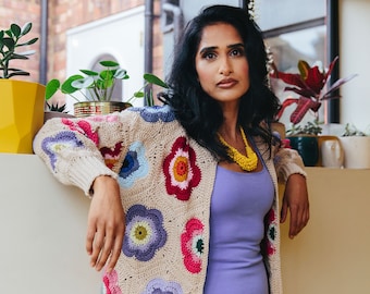 May include: A woman wearing a light purple dress and a crocheted cardigan with colorful flowers. The cardigan is beige with multi-colored flowers.