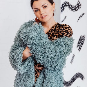 Könnte beinhalten: Eine Frau trägt einen hellblauen, flauschigen Cardigan über einem braunen und schwarzen Leopardenmusterkleid. Sie hat ihre Haare zu einem Dutt hochgesteckt.