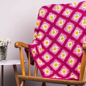 May include: A pink and white crocheted throw blanket with a daisy pattern. The blanket is draped over a wooden rocking chair.