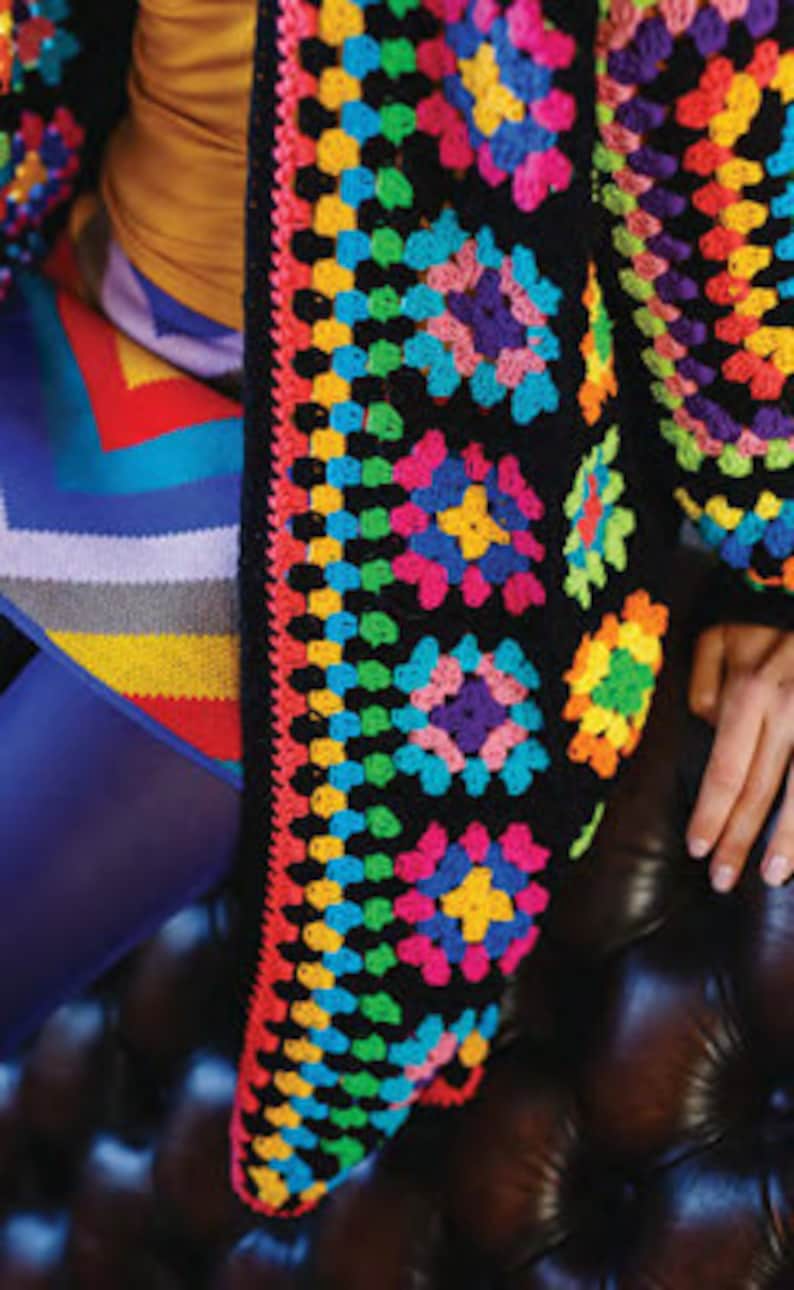 Puede incluir: Una chaqueta de punto de ganchillo negra con un patr&oacute;n de cuadrados de la abuela de colores. La chaqueta est&aacute; hecha con una variedad de colores brillantes, incluyendo rojo, naranja, amarillo, verde, azul y morado.