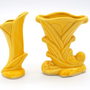 Może przedstawiać: Dwa żółte ceramiczne wazony z kwiatowym wzorem. Wazon po lewej stronie jest wysoki i smukły, podczas gdy wazon po prawej stronie jest niższy i szerszy.