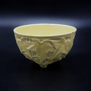 Puede incluir: Un tazón de cerámica amarillo con un diseño de hojas. El tazón tiene una forma redondeada y un borde ancho. Se encuentra sobre una superficie negra.