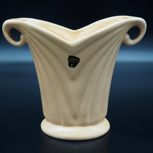 Może przedstawiać: Jasnożółty ceramiczny wazon z żebrowanym wzorem i dwoma uchwytami. Wazon ma etykietę z napisem "Camar Pottery".