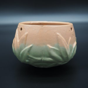 Puede incluir: Una maceta de cerámica de dos tonos. La parte superior es de color melocotón claro, que pasa a verde en la base. Tiene patrones en forma de hojas y dos pequeños agujeros cerca del borde.